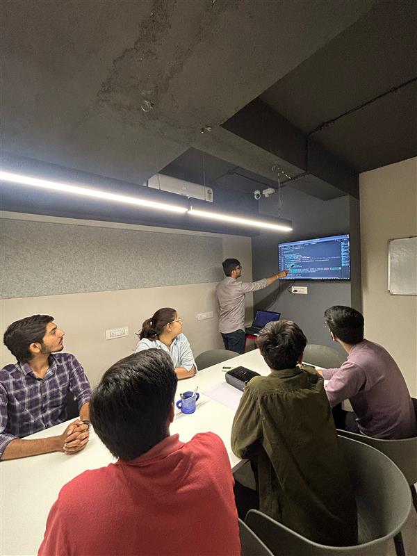 person writing in a notebook beside by an iPad, laptop, printed photos, spectacles, and a cup of coffee on a saucer